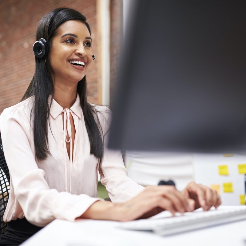 Female Customer Services Agent Working At Desk In Call Center